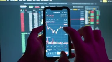 Cryptocurrency stock market on mobile phone screen.bA people sits at home with a laptop and phone, watching cryptocurrency trading.Stock market chart of Bitcoin currency. High quality 4k footage
