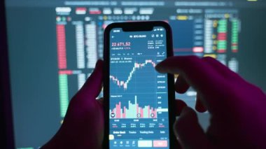 Trader using computer and mobile phone invests in cryptocurrency,stock market and stock exchange in a dark room.Scaling and analyzing the cryptocurrency chart on the phone screen.4k