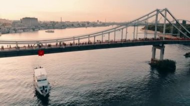 Aerial view of the pedestrian bridge across the Dnieper River.People walk on a pedestrian bridge with bike paths.A pleasure boat passes through the water under the bridge.High quality 4k footage