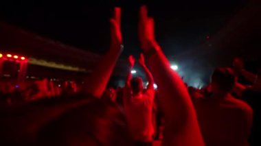 İnsanlar akşam konserinde ellerini çırpıp ışık gösterisiyle dans ediyorlar. Hayranlar sahnede parlak renkli flaş ışıklarıyla ellerini kaldırıyorlar. Kalabalık dans ediyor, müzik gruplarını çekiyor.