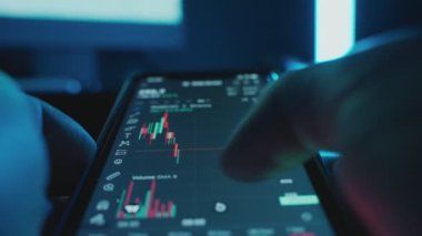 Bir tüccar karanlık bir odada şifreli para, borsa ve borsada cep telefonu yatırımları kullanıyor. Telefon ekranındaki kripto para şemasını ölçeklendirip analiz ediyorum. Yüksek kalite 4K görüntü.