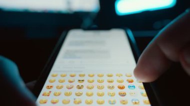 Dokunmatik ekranlı akıllı telefon kullanarak mesaj yazan bir kişi göndermek için bir emoji seçer. Mesaj yazma kavramı, sosyal medya iletişimi, SMS gönderme, notlar. Yüksek kalite 4k görüntü