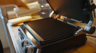 Evdeki mutfak masasında ısıtmalı ızgara açan bir kadın, daha fazla yemek pişirmek için üzerine lavaş döker. Elektrikli ızgarada ev yapımı lavash shawarma pişiriyorum. Yüksek kalite 4k görüntü