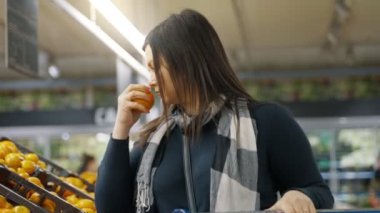 Elinde el arabası olan bir kız bir süpermarkette mandalina sergisine gider ve birkaç tane seçer. Bir kadın süpermarkette alışveriş yapıyor. 4k biçiminde yüksek kaliteli atış
