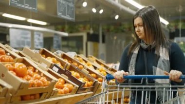 Kız süpermarketteki vitrindeki kutulara gider ve raftaki domatesleri seçer. Bir kadın süpermarkette alışveriş yapıyor. 4k biçiminde yüksek kaliteli atış