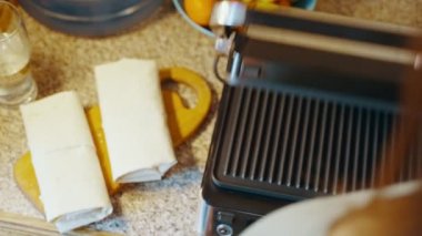 Evdeki mutfak masasında ısıtmalı ızgara açan bir kadın, daha fazla yemek pişirmek için üzerine lavaş döker. Elektrikli ızgarada ev yapımı lavash shawarma pişiriyorum. Yüksek kalite 4k görüntü