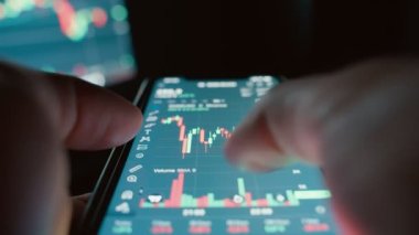 Cryptocurrency stock market on mobile phone screen.bA people sits at home with a laptop and phone, watching cryptocurrency trading.Stock market chart of Bitcoin currency. High quality 4k footage