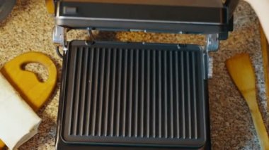 Evdeki mutfak masasında ısıtmalı ızgara açan bir kadın, lavaş ürününü daha fazla pişirmek için üzerine yerleştiriyor. Elektrikli ızgarada ev yapımı lavaş shawarma pişiriyor. Yüksek kalite 4k görüntü