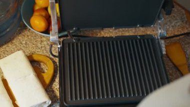 Evdeki mutfak masasında ısıtmalı ızgara açan bir kadın, daha fazla yemek pişirmek için üzerine lavaş döker. Elektrikli ızgarada ev yapımı lavash shawarma pişiriyorum. Yüksek kalite 4k görüntü
