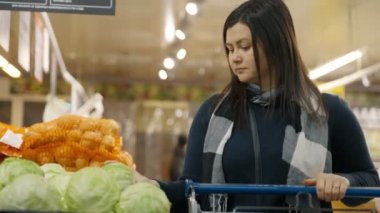 Bir kadın süpermarketin camına doğru yürür ve çekmeceden yeşil lahana seçer. Bir kadın süpermarkette alışveriş yapıyor. 4k biçiminde yüksek kaliteli atış