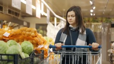 Bir kız süpermarket vitrinine gider ve bir lahana seçer. Bir kadın süpermarkette alışveriş yapıyor. 4k biçiminde yüksek kaliteli atış
