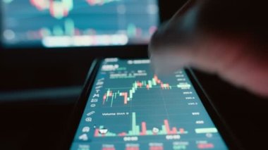 Cryptocurrency stock market on mobile phone screen.bA people sits at home with a laptop and phone, watching cryptocurrency trading.Stock market chart of Bitcoin currency. High quality 4k footage