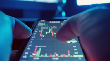 Cryptocurrency stock market on mobile phone screen.bA people sits at home with a laptop and phone, watching cryptocurrency trading.Stock market chart of Bitcoin currency. High quality 4k footage