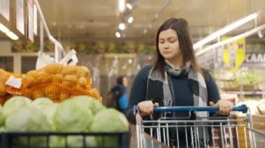 Bir kadın süpermarketin camına doğru yürür ve çekmeceden yeşil lahana seçer. Bir kadın süpermarkette alışveriş yapıyor. 4k biçiminde yüksek kaliteli atış