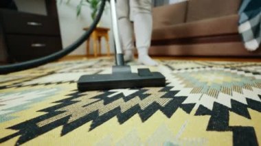 Tanımlanamayan bir ev hanımı, kirli ve tozlu bir halıyı elektrikli süpürgeyle süpürüyor. Modern ev temizliği kavramı.