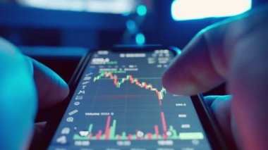 Bir tüccar karanlık bir odada şifreli para, borsa ve borsada cep telefonu yatırımları kullanıyor. Telefon ekranındaki kripto para şemasını ölçeklendirip analiz ediyorum. Yüksek kalite 4K görüntü.