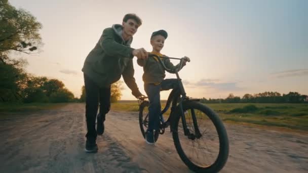 Старший Брат Учит Младшего Брата Кататься Велосипеде Закате Веселые Выходные — стоковое видео