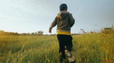 Mutlu bir çocuk çimlerin üzerindeki bir çayırda eğleniyor ve eğleniyor. Çimlerin üzerindeki bir tarlada güneş ışınlarında bir çocuk. Yüksek kalite 4k görüntü