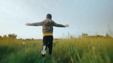 Neşeli ve neşeli bir çocuk güneşli bir günde yeşil çimlerin üzerinde dikkatsizce koşar. Mutlu bir çocukluk. Çimlerin üzerindeki bir tarlada güneş ışınlarında bir çocuk. 4k biçiminde yüksek kaliteli atış