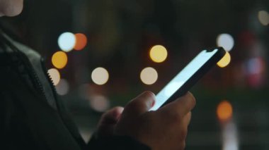 Kadınların elleri telefonu tutuyor, sosyal ağlarda parmaklarıyla haberleri inceliyor. Gece şehri, güzel Bokeh. Yüksek kalite 4k görüntü