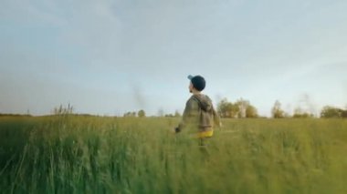 Neşeli bir çocuk güneşli bir günde yeşil çimlerin üzerinde koşar. Çocuk oyunu. Mutlu bir çocukluk. Çimlerin üzerindeki bir tarlada güneş ışınlarında bir çocuk. Yüksek kalite 4k görüntü