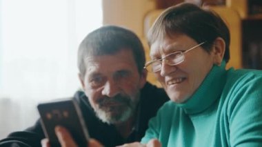 Mutlu yaşlı bir çift cep telefonuyla video görüşmesi yapıyor ya da sevdiklerinin resimlerine bakıyor. Yaşlı ebeveynler çocuklarını videoda gördüklerine seviniyorlar.
