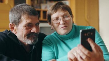 Oturma odasında oturan yaşlı bir çift cep telefonundan bir şeye bakıyor, tartışıyor ve gülüyorlar. Ebeveynler. Yüksek kalite 4k görüntü