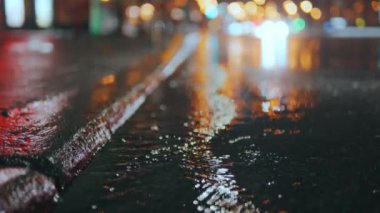 Çamurlu bir su birikintisine basan ve su sıçratan bir kadının hızlandırılmış görüntüsü. Su birikintisinden akan yağmur damlaları lense sıçrıyor. Yağmurlu bir gece şehri. Yüksek kalite 4k görüntü