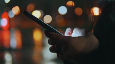 Kadın elleri telefonu tutuyor, sosyal ağlarda haberlere parmak izleriyle bakıyor. Mesajlaşma. Gece şehri, güzel Bokeh. 4k biçiminde yüksek kaliteli atış