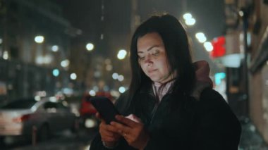 Şehirde genç bir kız elinde şemsiyeyle geçen arabaların arka planına karşı duruyor, yağmurdan saklanıyor ve cep telefonu 45 'liğinin ekranına bir mesaj yazıyor.