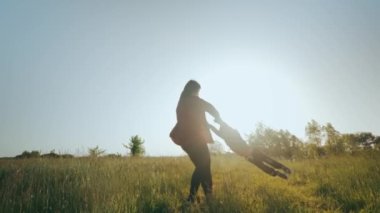 Genç bir anne oğluyla dışarıda oynar, etrafında döner ve eğlenir. Ebeveynler ve küçük çocuklar sahada birlikte oynuyorlar. Hayatın mutlu anları. Yüksek kalite 4k görüntü