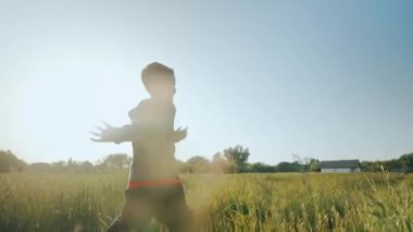 Neşeli bir çocuk güneşli bir günde yeşil çimlerin üzerinde koşar. Çocuk oyunu. Mutlu bir çocukluk. Çimlerin üzerindeki bir tarlada güneş ışınlarında bir çocuk. Yüksek kalite 4k görüntü