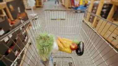 Timelapse of filling a shopping cart with various food products in a supermarket. Moving between different aisles in a large supermarket, various useful products are placed in turn in the cart.4k