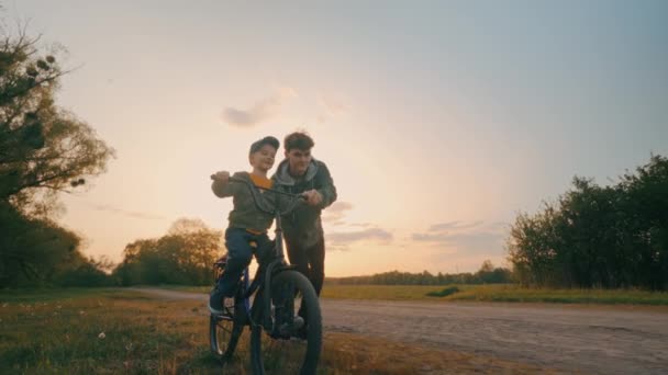 Fröhliche Brüder Lernen Bei Sonnenuntergang Fahrrad Fahren Der Ältere Bruder — Stockvideo