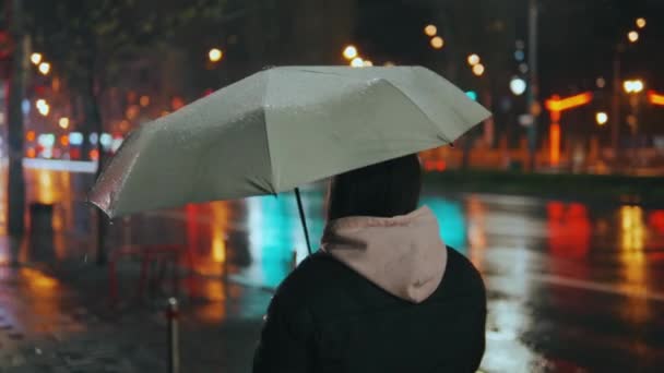 Young Woman Uses Smartphone While Holding Umbrella While Walking Outdoors — Stock Video