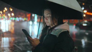 Şehirde genç bir kız elinde şemsiyeyle geçen arabaların arka planına karşı duruyor, yağmurdan saklanıyor ve cep telefonu 45 'liğinin ekranına bir mesaj yazıyor.