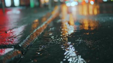 Soyut yağmurlu gece modern şehir, kaldırım kenarındaki su birikintisine adım atan kız. Islak ayakkabılar. Yağmurlu şehir. Yağmur damlaları sokak lambalarıyla aydınlatılan çok renkli asfalta düşer. Yüksek kalite 4k görüntü