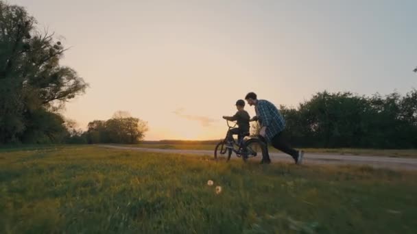 Tipo Feliz Enseña Hermano Pequeño Andar Bicicleta Una Carretera Rural — Vídeos de Stock