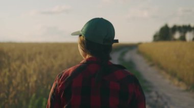 Bir çiftçi kadın buğday tarlasının yakınındaki toprak yolda yürüyor, toprağı ve buğday ekinlerini inceliyor. İş kadını tahıl hasadını analiz ediyor. Tarım işi. Ekolojik. Yüksek kaliteli 4K video kaydı.