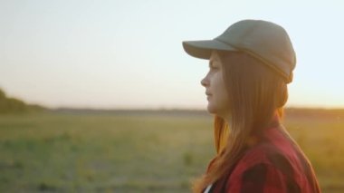Şapkalı bir kadın gün batımında tarlada yürüyor tarlaları ve yeşil tarlaları teftiş ediyor. İş gününün sonunda. Tarlada bir yürüyüş. Tarım sektörü konsepti. 4k biçiminde yüksek kaliteli atış