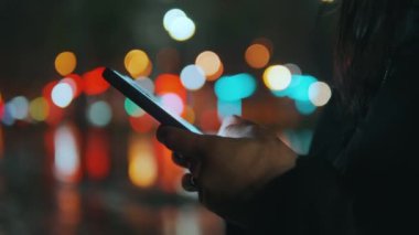 Kadın elleri ve arka planda ışık olan akıllı telefon ekranının görüntüsü. Kız cep telefonu kullanıyor, akıllı telefondan mesajlaşıyor. Yüksek kalite 4k görüntü