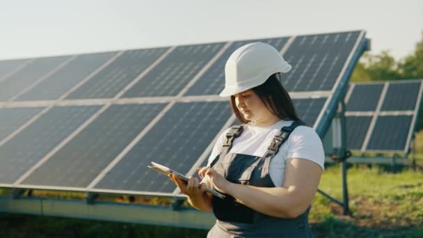 一位女工程师和她的助手头戴硬礼帽 手持平板电脑 检查太阳能电池板的安装情况 — 图库视频影像
