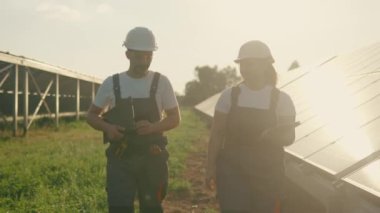 Bir kız mühendis ve asistanı fotovoltaik güneş panellerini inceleyerek yeşil enerji ve yenilenebilir enerjinin sonuçlarını inceliyorlar. Güneş enerjisi santralinde yeşil enerji kavramı.