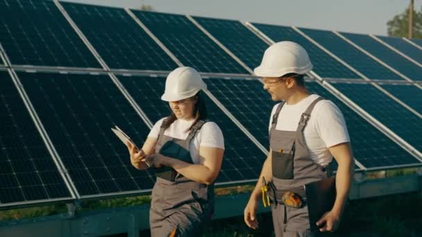 一位女工程师和他的助手走过光伏太阳能电池板 分析绿色能源和可再生能源的成果 太阳能发电厂中的绿色能源概念 — 图库视频影像