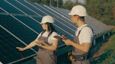 Bir kadın mühendis ve üniformalı bir işçi güneş panellerini kontrol ediyor. Enerji tasarrufu projesi üzerinde çalışıyorlar. İşçiler, sistemin etkinliğini tartışıyor ve odaklanıyor. 