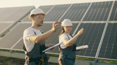 Bir kız mühendis ve asistanı fotovoltaik güneş panellerini inceleyerek yeşil enerji ve yenilenebilir enerjinin sonuçlarını inceliyorlar. Güneş enerjisi santralinde yeşil enerji kavramı.