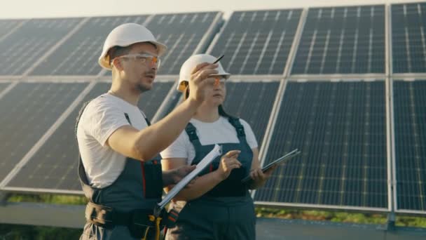 一位女工程师和一位穿着制服的工人正在检查太阳能电池板 他们正在做一个节能工程 工人们聚精会神地讨论系统的有效性 — 图库视频影像