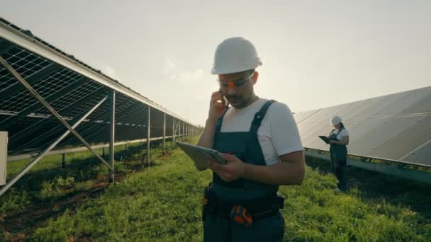 太陽光発電所の近くで電話で話し メモ帳からデータを送信する労働者の肖像画 太陽光発電プラントの効率化 4Kフォーマットでの高品質撮影 — ストック動画