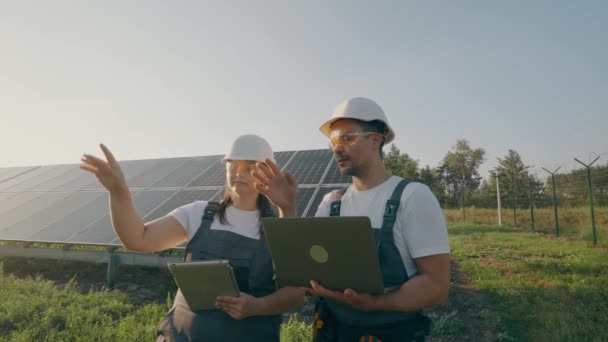 ソーラーパネルの動作を確認しながら 安全ヘルメットやベストで有能なエンジニアのリアビュー 男女共通のグリーンエネルギープロジェクトで協力しています — ストック動画