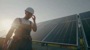 Belgeleri olan bir erkek işçi güneş paneli istasyonunda çalışıyor. Elektrik üretim sisteminin işleyişini izliyoruz. Yeşil elektrik konsepti. Yüksek kalite 4K görüntü